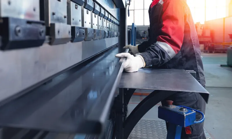 Male worker operating industrial metal press brake in factory setting, banner.