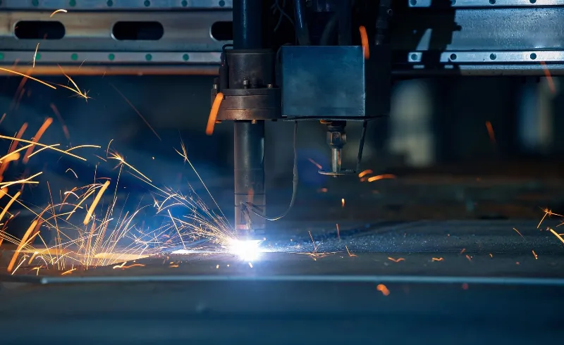 Plasma cutting machine cuts metal material with sparks, industrial background.